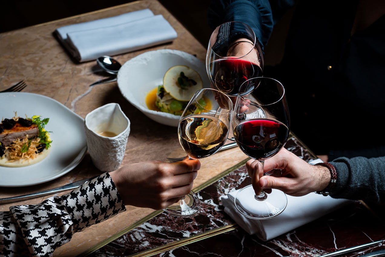 3 wine glasses cheers over a dinner table, dimly lit